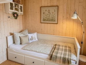 Ein Schlafzimmer mit einem Bett, einer Nachttischlampe, einem Regal mit Dekoration und einem gerahmten Pflanzenmotiv an der Wand.