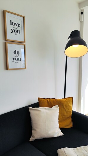 A room with a black sofa, two cushions, a black floor lamp, and two framed inspirational quotes on the wall. - Arena Home, Chic, and Sea View. Next to the port of Corralejo (Corralejo)