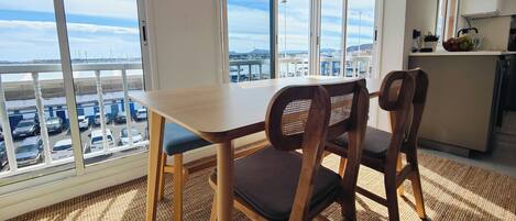 Una habitación con vista a un puerto deportivo, una mesa de comedor, dos sillas y una zona de cocina.