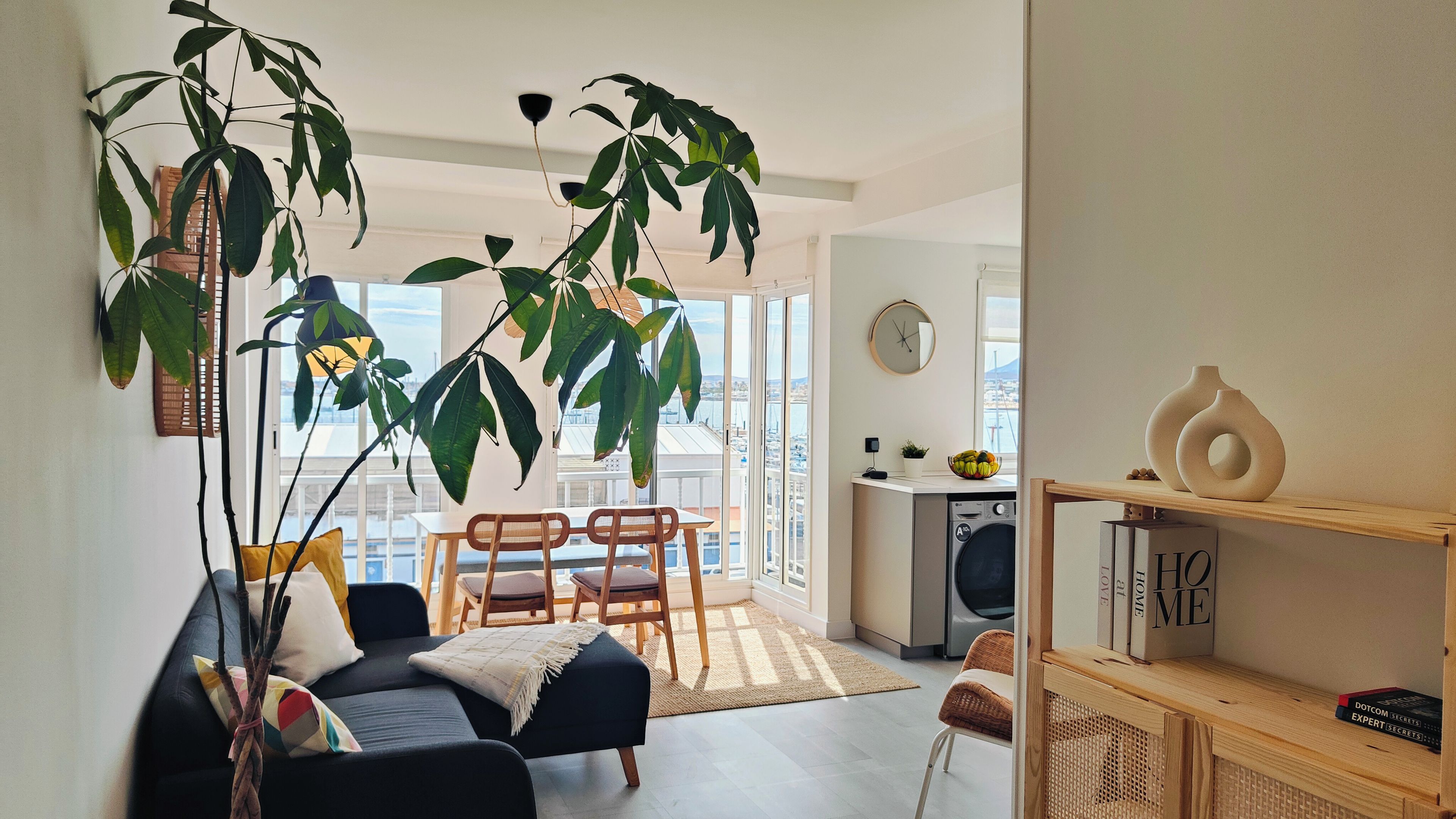 A modern living room with a sofa, chairs, a dining table, and a kitchen area with a washing machine.