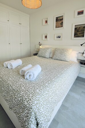 A bedroom with a large bed, white walls, and a ceiling light. - Arena Home, Chic, and Sea View. Next to the port of Corralejo (Corralejo)
