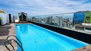 Una piscina en la azotea con barandilla de cristal, una estructura parecida a una carpa y vistas a la ciudad.