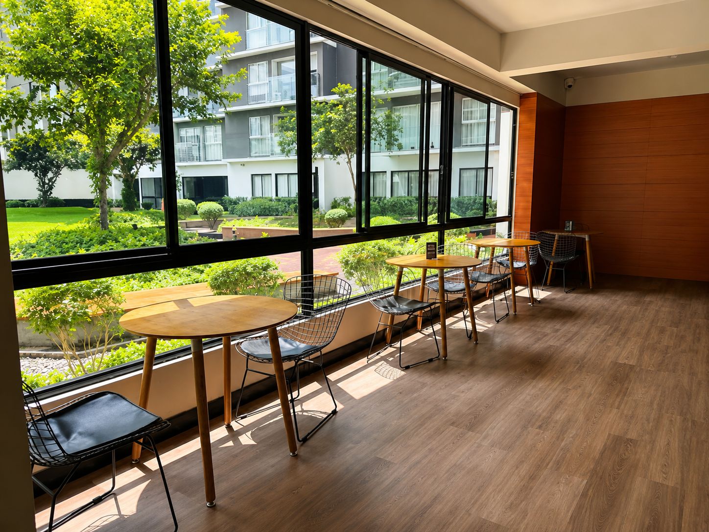 Un interior moderno con ventanas amplias, suelo de madera y una zona de estar con mesas y sillas.