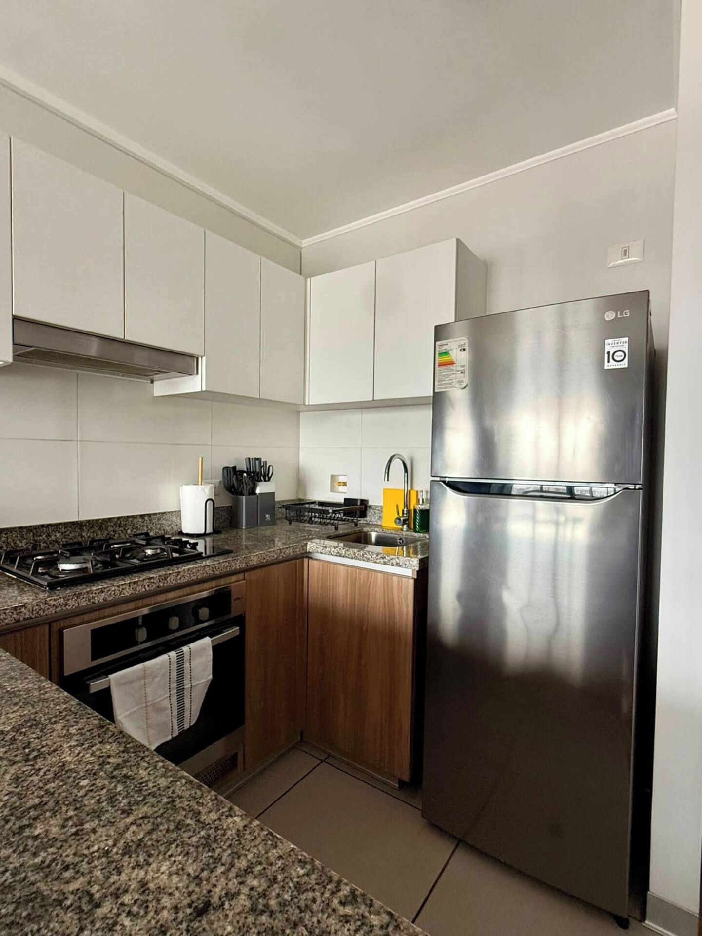 A modern kitchen with white cabinets, a stainless steel refrigerator, a gas stove, and a wooden countertop.
