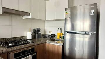 A modern kitchen with white cabinets, a stainless steel refrigerator, a gas stove, and a wooden countertop.