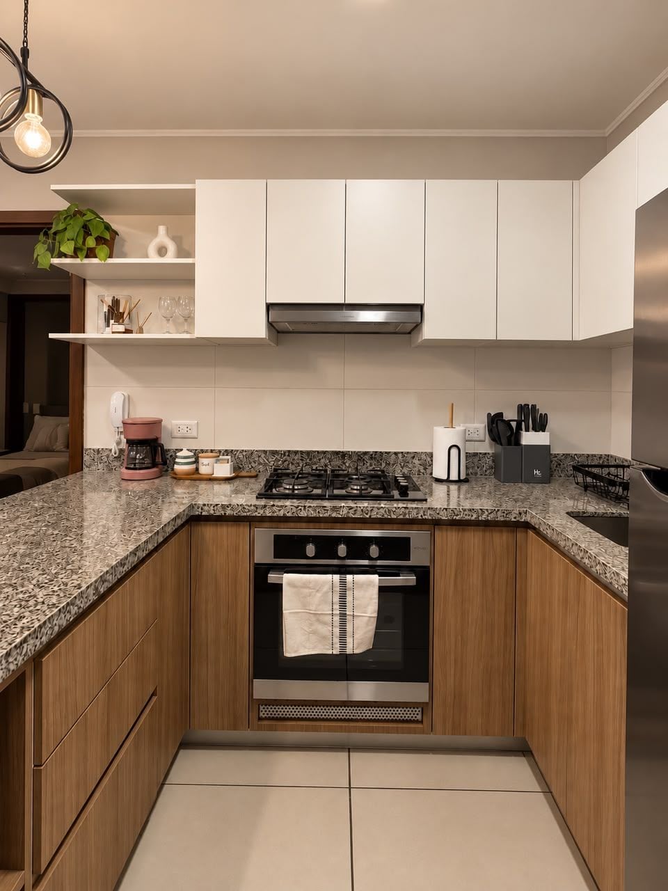 Una cocina moderna con armarios blancos, encimera de granito, electrodomésticos de acero inoxidable y una lámpara colgante.