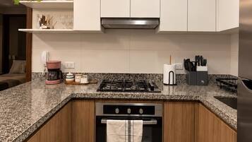 Una cocina moderna con armarios blancos, encimera de granito, electrodomésticos de acero inoxidable y una lámpara colgante.