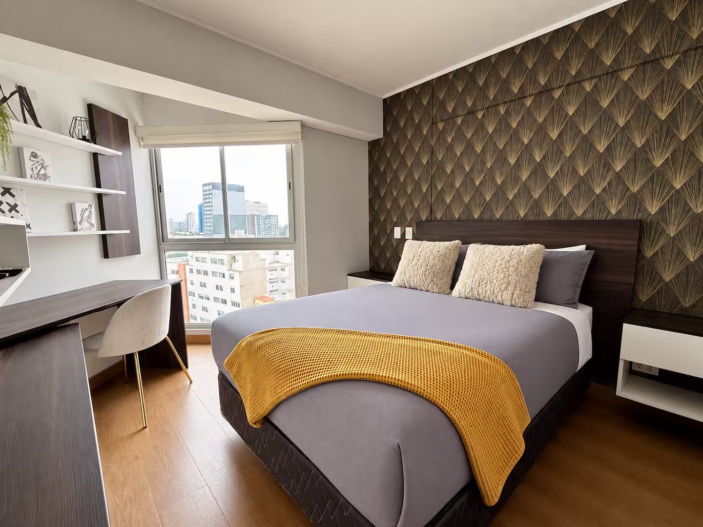 A modern bedroom with a bed, a desk, and a city view.