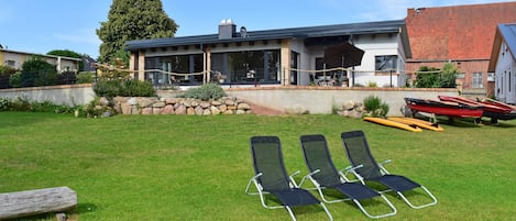 A modern house with a covered patio, a stone wall, and a grassy lawn.