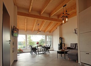 A spacious kitchen with wooden beams, a dining area with chairs and a table, and a sofa. - Bungalow mit Seeblick in Klein Labenz (Warin)