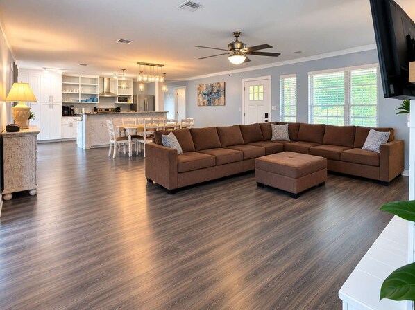 A modern living room with a sectional sofa, a dining area, and a kitchen in the background.
