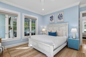 Un dormitorio con una cama blanca, dos lámparas de noche, una mesita de noche y un aparador azul.