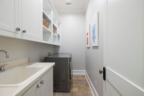 A narrow hallway with a white sink, a washing machine, and a door with a brass handle. - LSV | Private Pool | Outdoor Fireplaces (Santa Rosa Beach)