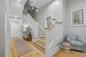 Eine Treppe mit Holzstufen und weißen Geländern, eine graue Wand mit einem gerahmten Gemälde und ein gemustertes Sofa.