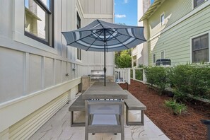 Eine Terrasse mit Grill, Tisch und Sonnenschirm.
