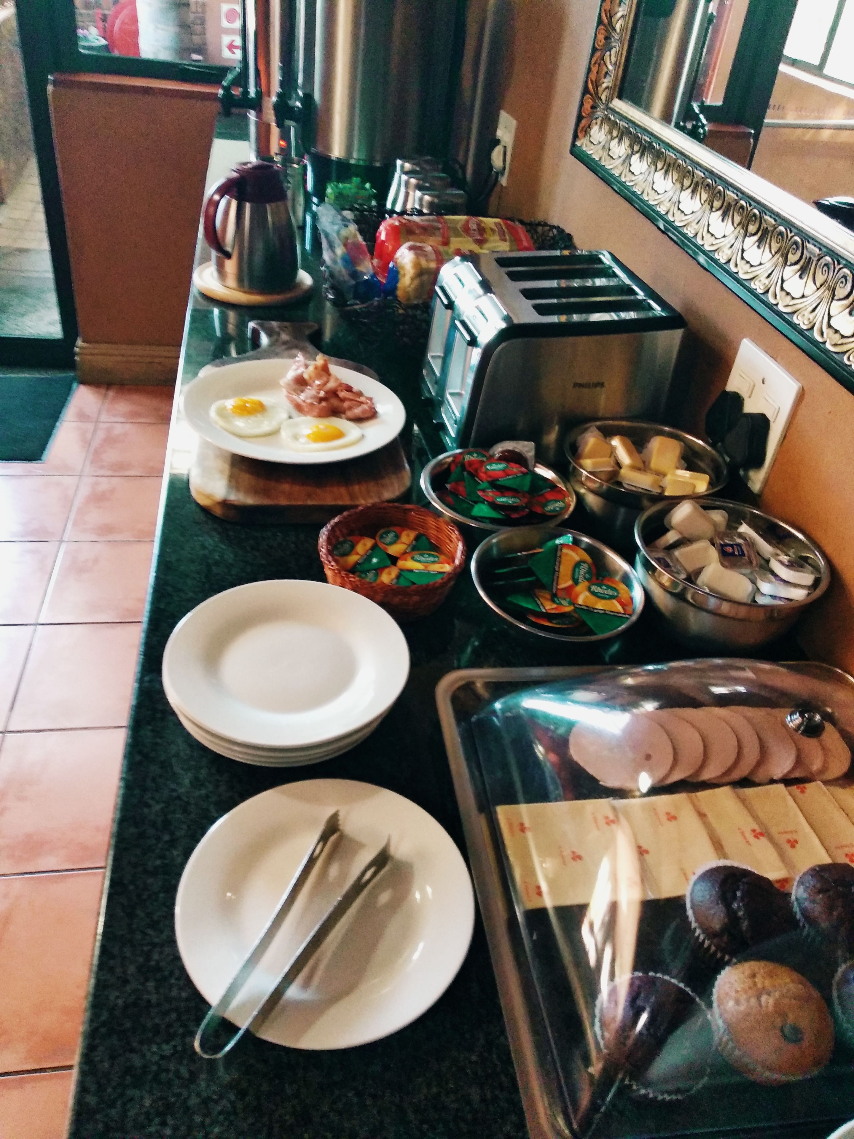 A breakfast buffet setup with various food items, utensils, and a toaster on a kitchen counter.