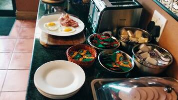 A breakfast buffet setup with various food items, utensils, and a toaster on a kitchen counter.