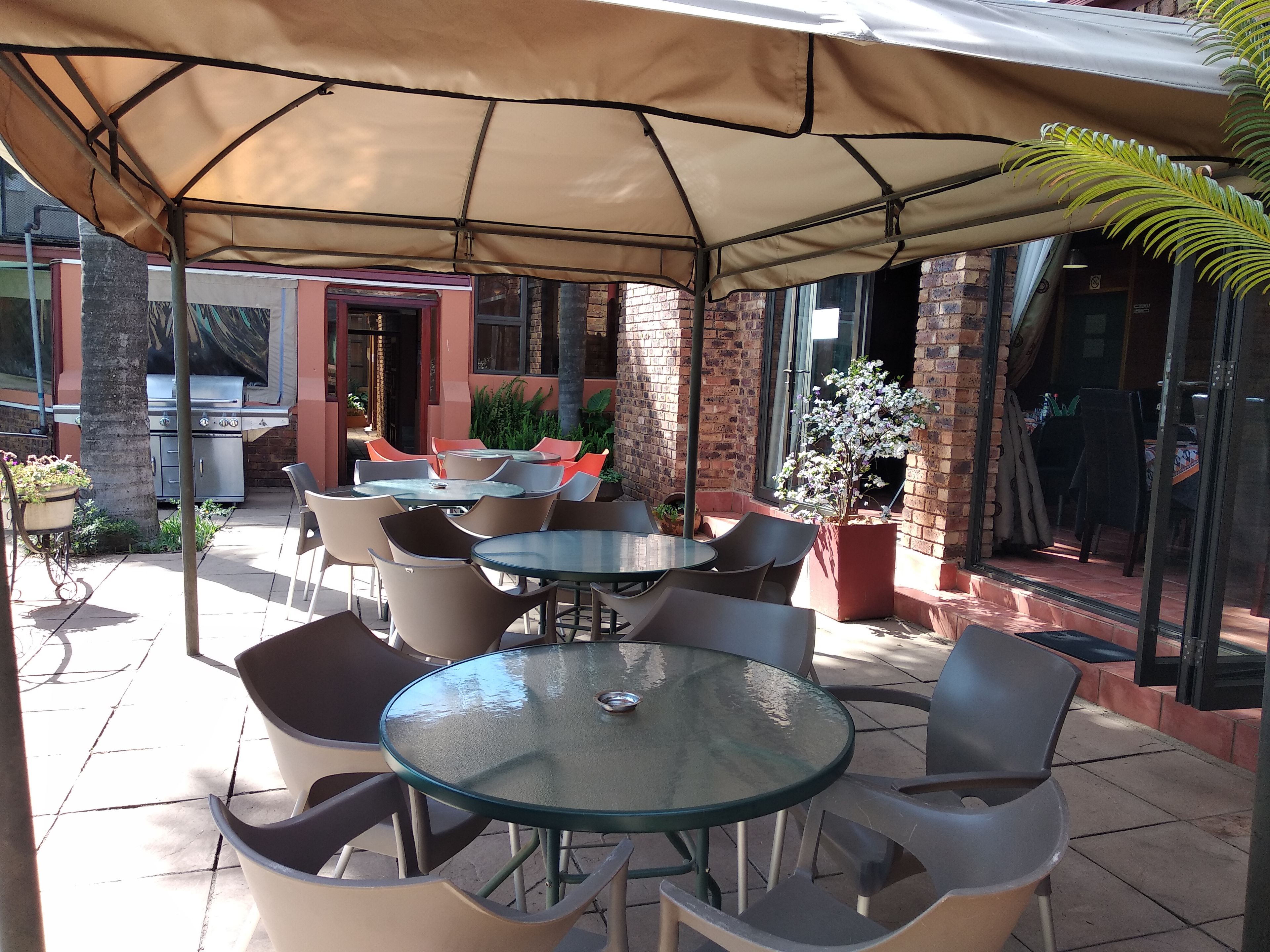 Un espacio patio al aire libre con mesas y sillas redondas, una parrilla y plantas en macetas.