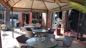 En udendørs terrasse med runde borde og stole, grill og krukker med planter.