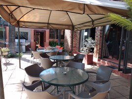 Un espacio patio al aire libre con mesas y sillas redondas, una parrilla y plantas en macetas.