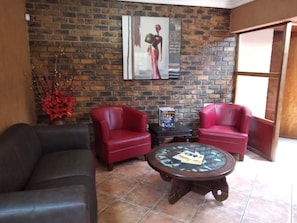 Uma sala de estar com parede de tijolos, dois sofás de couro vermelho, uma mesa de centro de vidro e um quadro.