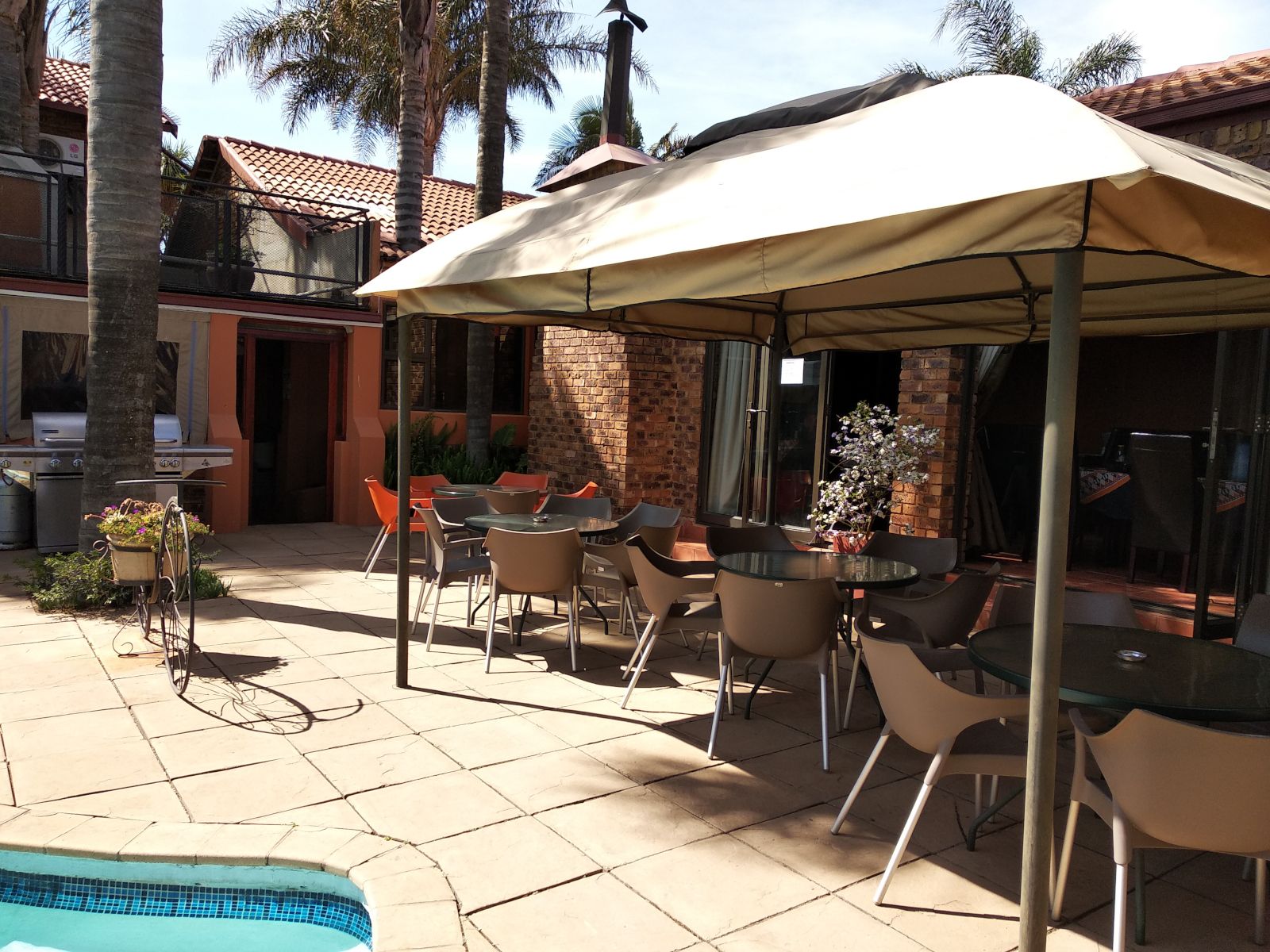Un patio exterior con piscina, zona de estar cubierta y una parrilla.