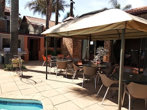 Une terrasse extérieure avec une piscine, un espace salon couvert et un barbecue.
