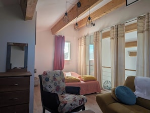 Ein Schlafzimmer mit einem Bett, einem Sessel, einem Sofa, einem Schminktisch und einem Fenster mit Vorhängen.