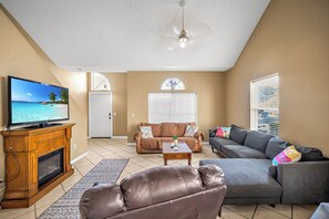 A living room with a television, sofas, a fireplace, and a ceiling fan. - The Retro Cove: Minutes to beach, 2 Pools (Panama City Beach)
