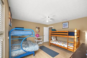A room with two bunk beds, a ceiling fan, a door, and a small shelf with toys. - The Retro Cove: Minutes to beach, 2 Pools (Panama City Beach)
