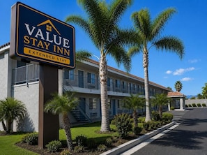 A Value Stay Inn Extended Stay hotel with a signboard, palm trees, and a clear sky. - Studio6 Hemet, CA (Hemet)