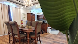 A dining area with a wooden table and chairs, a chandelier, and a large green plant. - Atlantic Suites Luxury Apartments (Anna Regina)