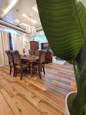 Un coin repas avec une table et des chaises en bois, un lustre et une grande plante verte.