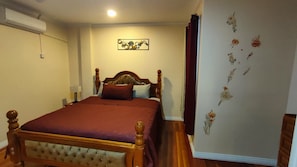 Une chambre avec un lit en bois, un climatiseur fixé au mur et des motifs floraux décoratifs sur les murs.