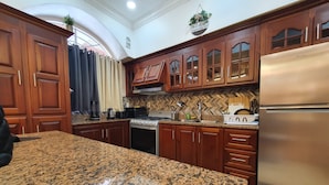A kitchen with granite countertops, wooden cabinets, a stainless steel refrigerator, and a herringbone backsplash. - Atlantic Suites Luxury Apartments (Anna Regina)