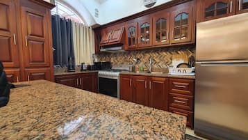 A kitchen with granite countertops, wooden cabinets, a stainless steel refrigerator, and a herringbone tile backsplash.