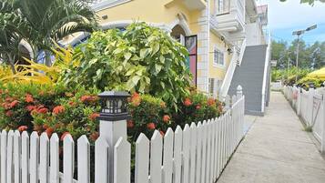 Um edifício de dois andares com cerca branca, varanda com balaústres brancos e escadaria que leva ao andar superior.