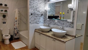 A bathroom with a toilet, shower, two sinks, a mirror, and a towel rack. - Atlantic Suites Luxury Apartments (Anna Regina)