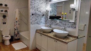 Une salle de bain comprenant des toilettes, une douche, deux lavabos, un miroir et un porte-serviettes.