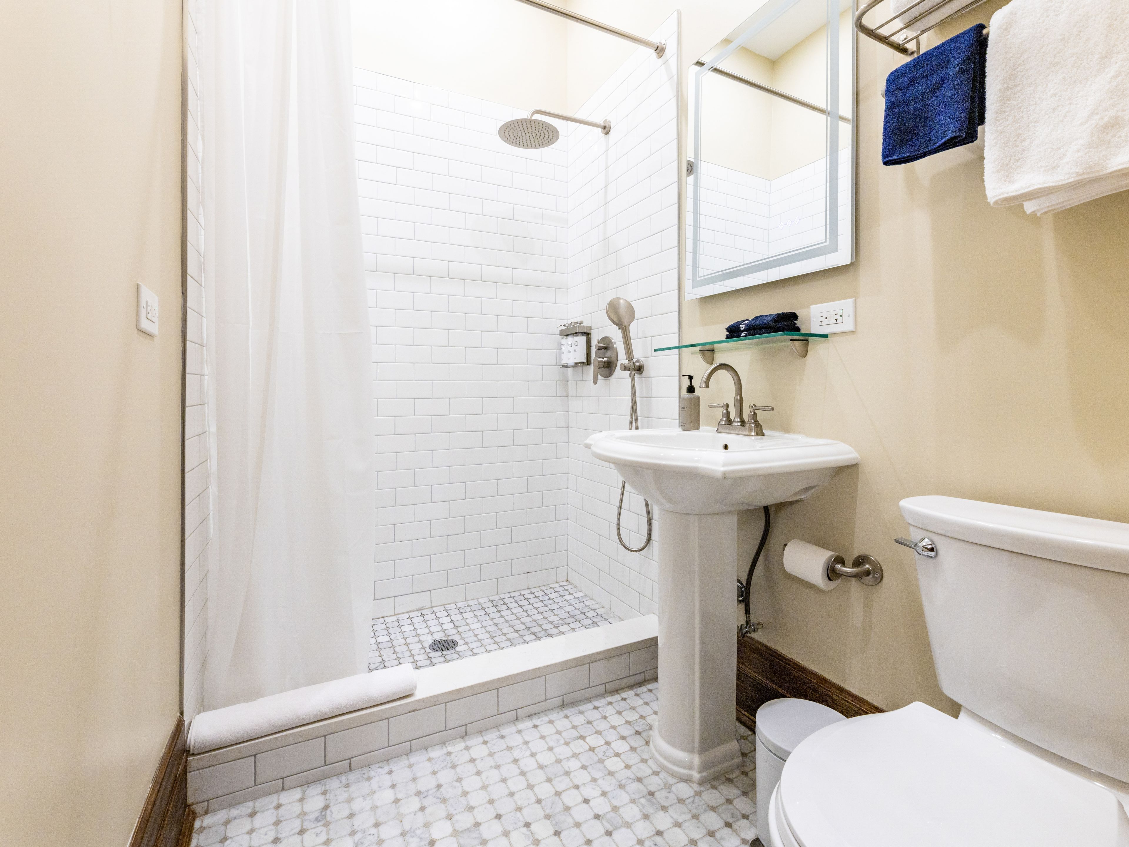A bathroom with a shower, sink, toilet, and a glass shelf.