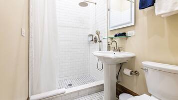 A bathroom with a shower, sink, toilet, and a glass shelf.