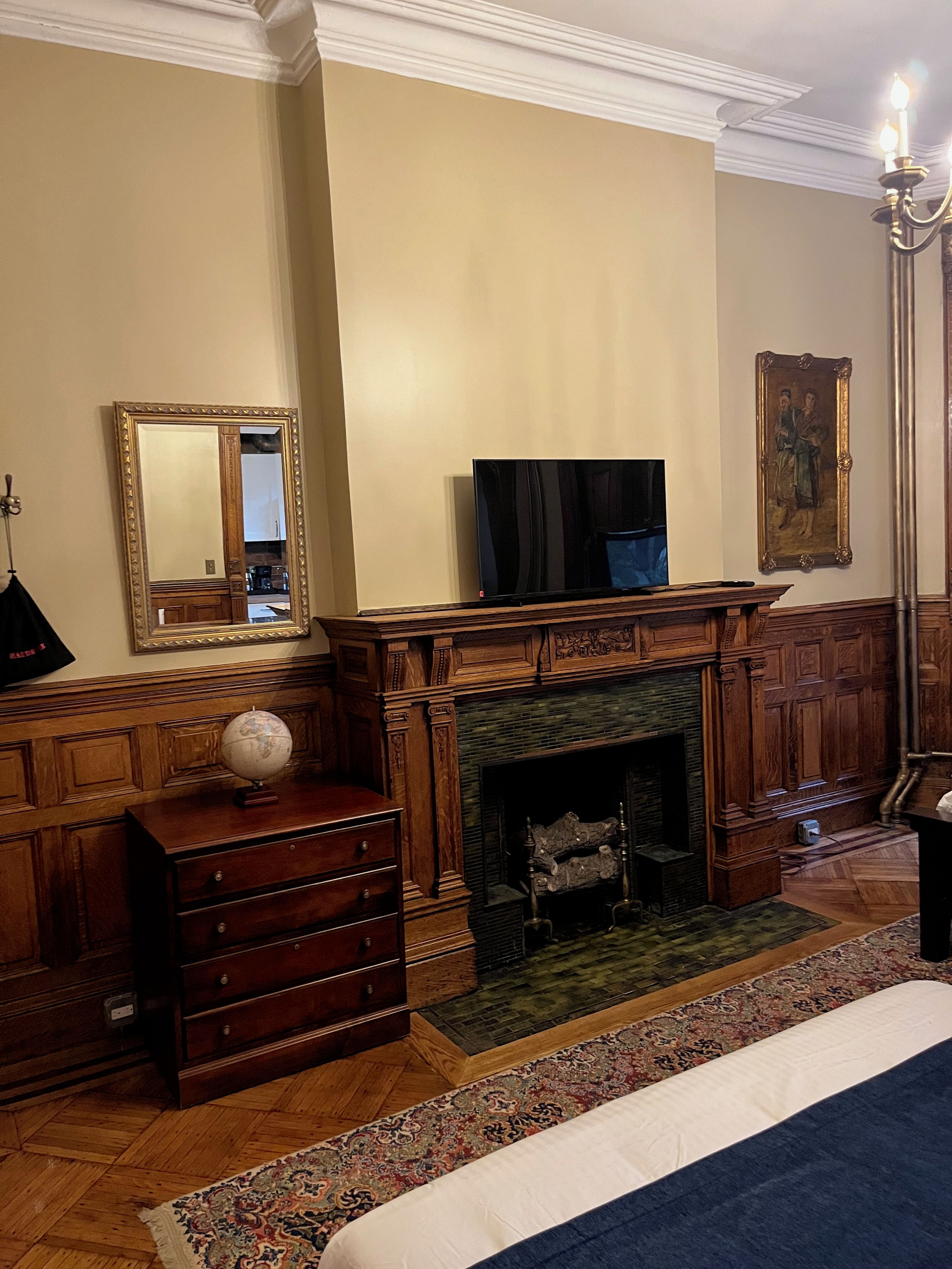 A room with a fireplace, a television, a globe on a dresser, and a large mirror.