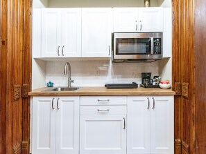 A kitchen with white cabinets, a stainless steel sink, a microwave, and a coffee maker.