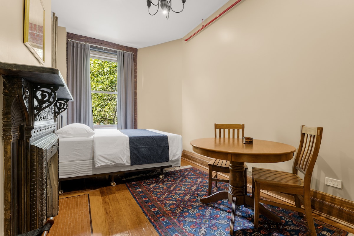 A room with a bed, a table with chairs, a patterned rug, and a chandelier.