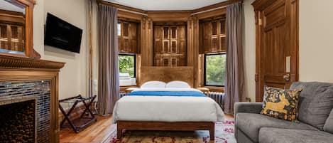 A bedroom with a large bed, a fireplace, a television, and a view of greenery outside.