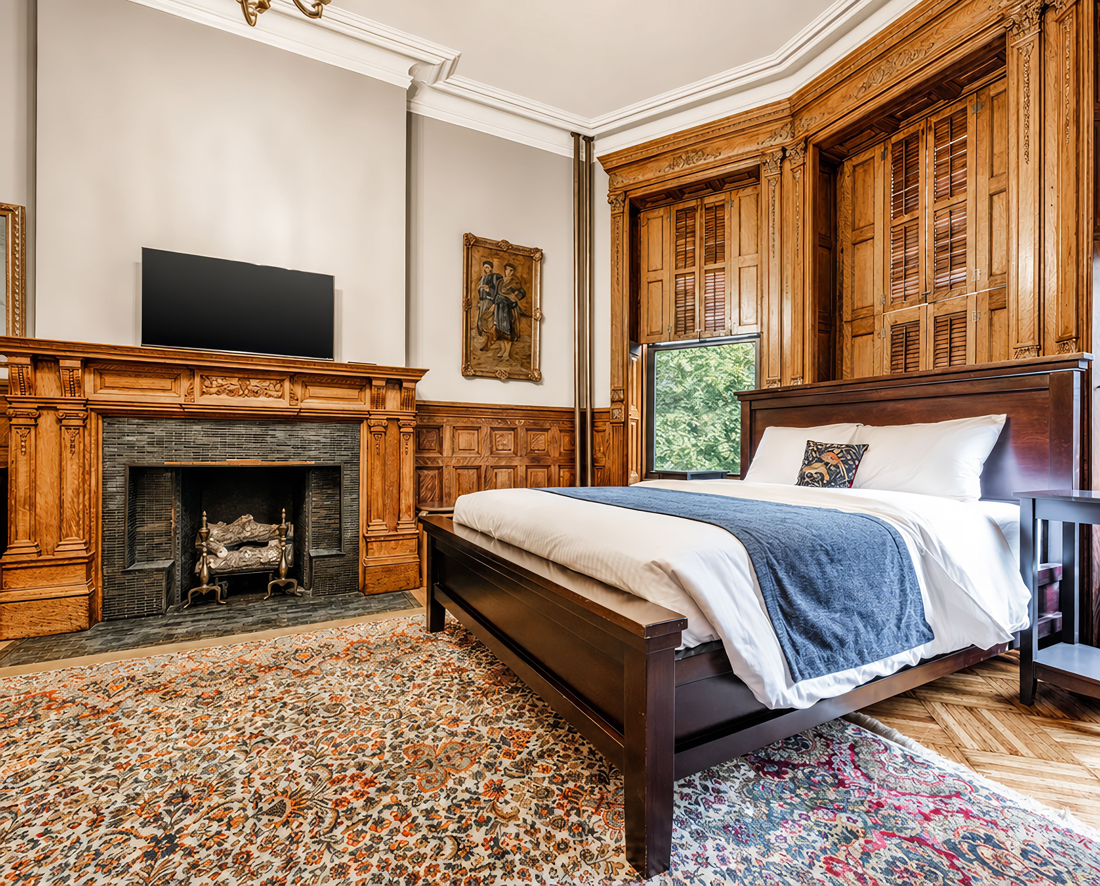 A bedroom with a large bed, a fireplace, wooden paneling, and a television.