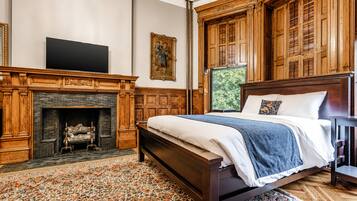 A bedroom with a large bed, a fireplace, wooden paneling, and a television.