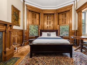 A traditional bedroom with a large bed, wooden paneling, and a view of greenery through the windows. - The Hamilton House Inn (New York)