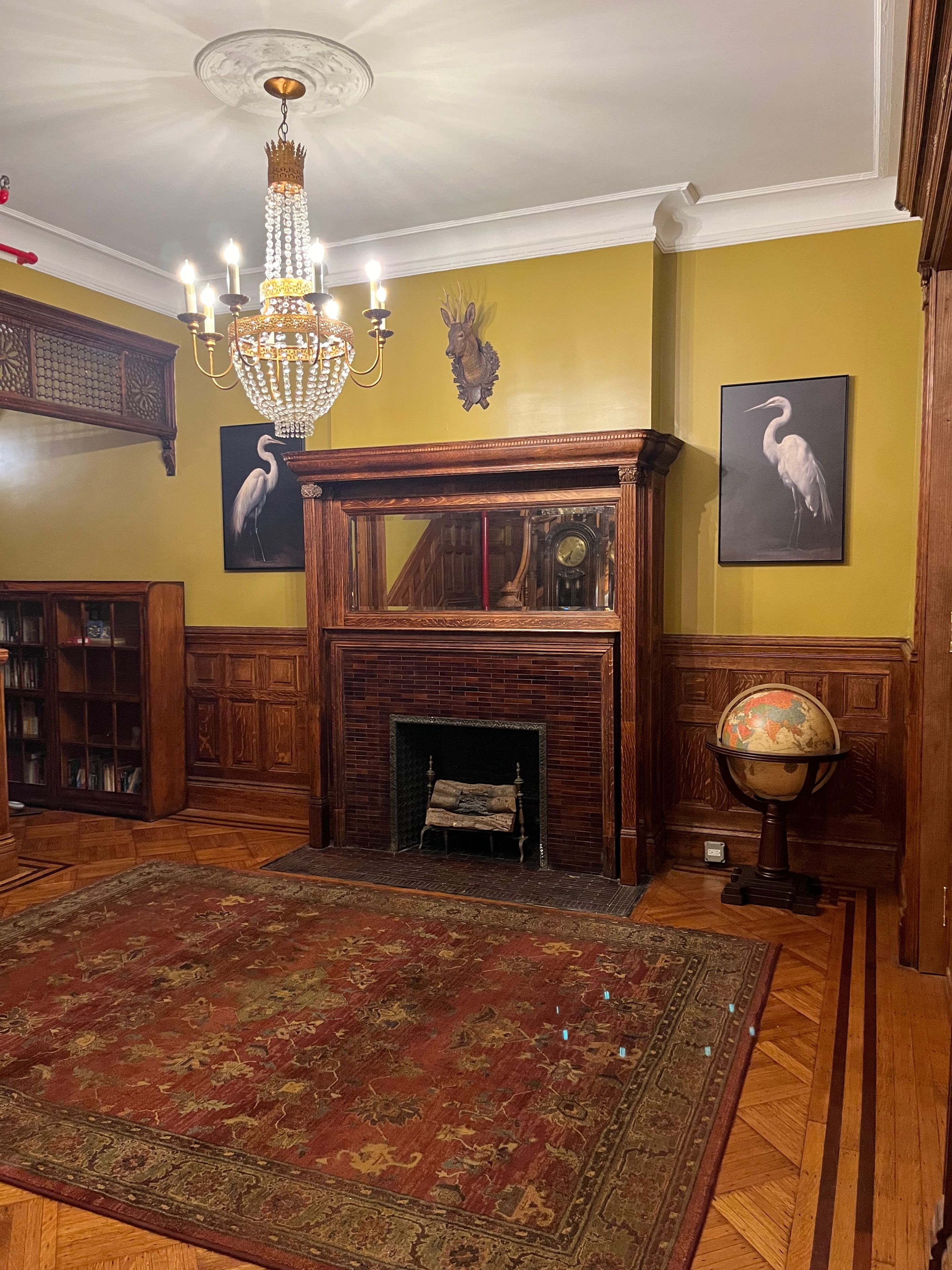 Quarto com lareira, um candelabro, um globo terrestre e estante de livros.