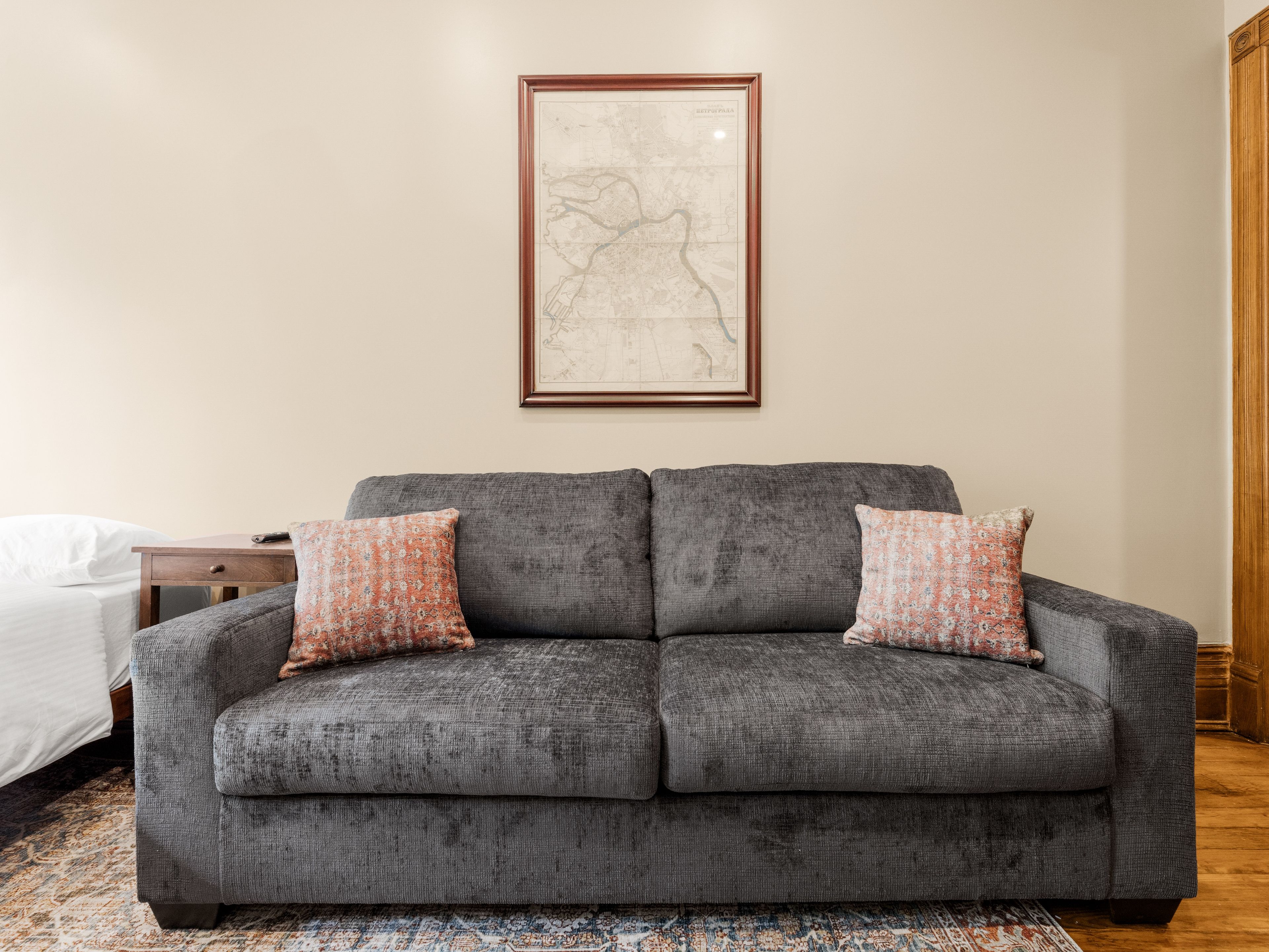 A grey sofa with floral cushions, a framed map on the wall, and a patterned rug.